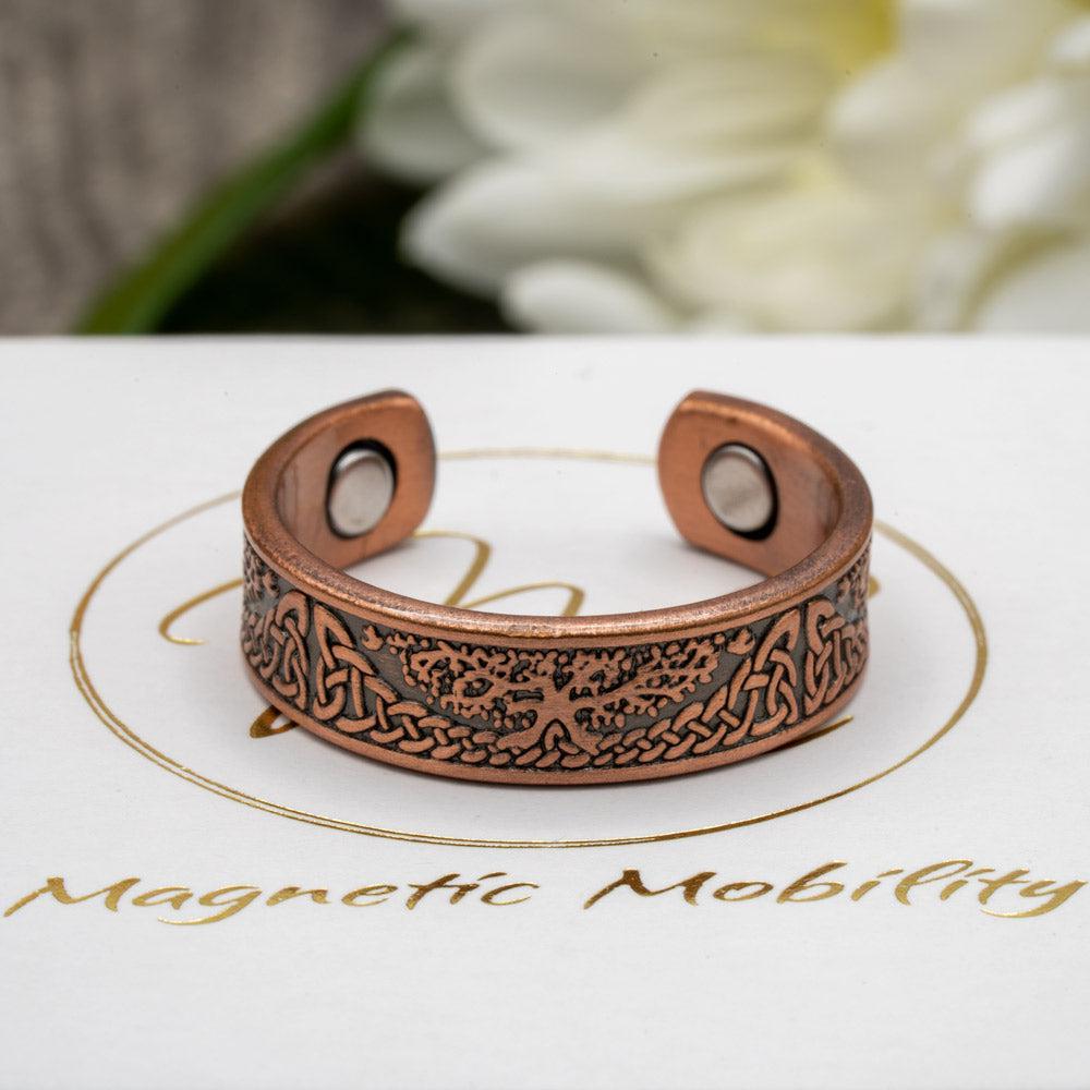 Close-up of Buckthorn copper ring with Tree of Life design from Magnetic Mobility, displayed on branded packaging. The open back allows for easy adjustment on arthritic fingers, combining elegance and practicality.