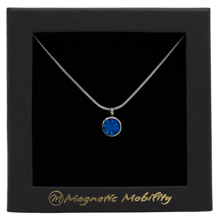 December Magnetic Mobility Birthstone Necklace featuring a Blue Swarovski crystal pendant with a magnetic back. Ideal for relieving neck pain, displayed in a black box with Magnetic Mobility logo